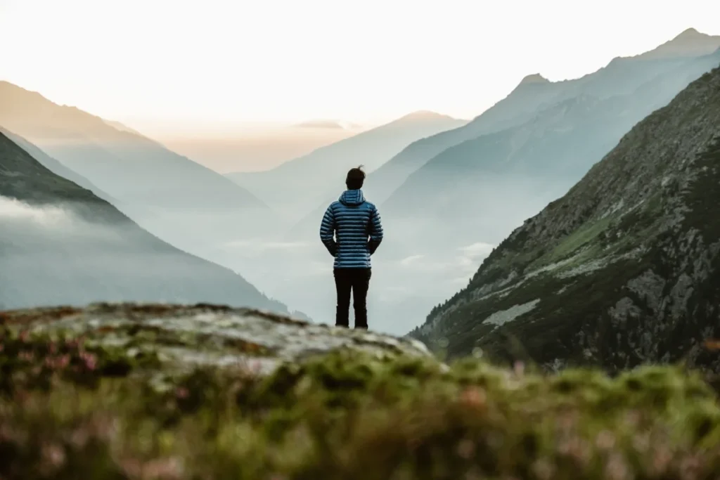 Person overlooking a scenic landscape, putting away their smartphone, symbolizing digital detox travel