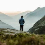 Person overlooking a scenic landscape, putting away their smartphone, symbolizing digital detox travel